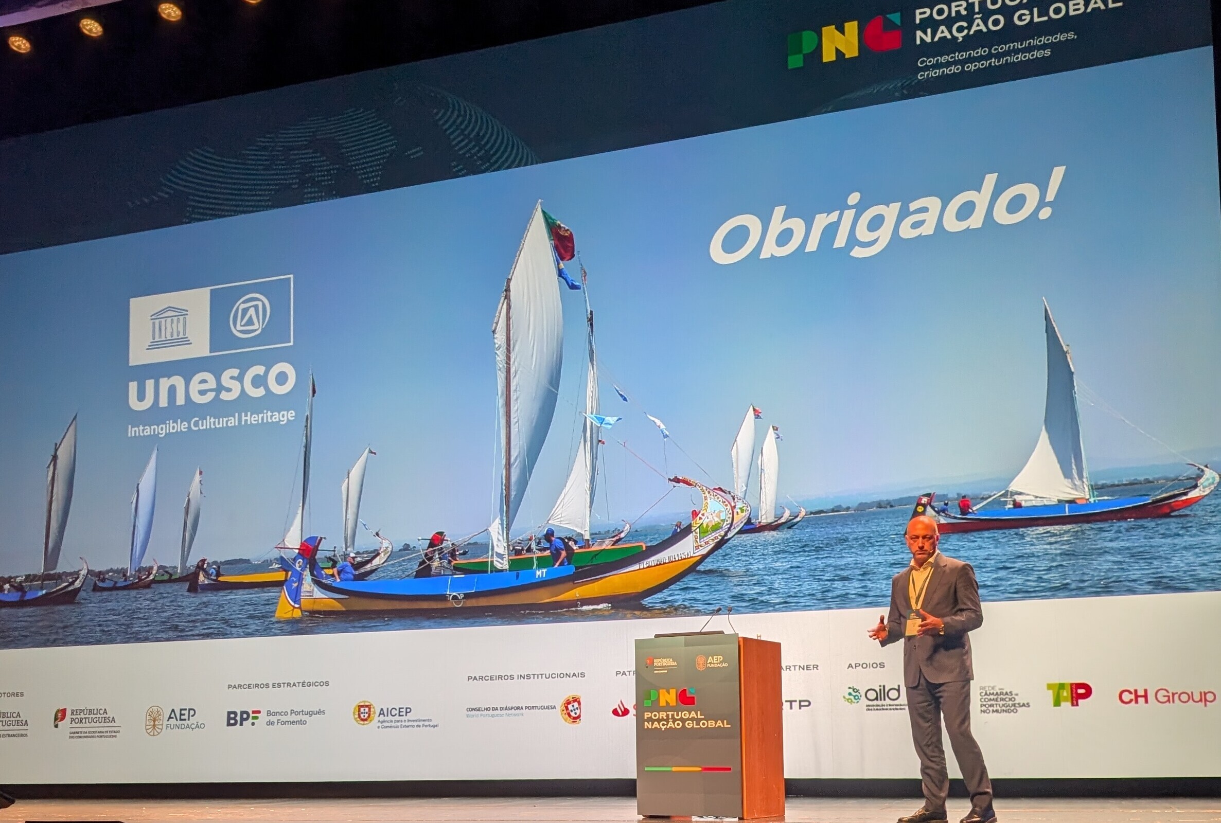 Um participante em pé, no palco, com ecrã de apresentação ao fundo. Participante: Luís Souto de M...